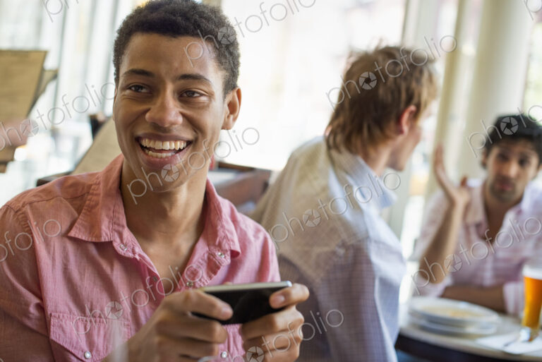 Urban Lifestyle. Three young men in a cafe. One checking his smart phone. Two talking…