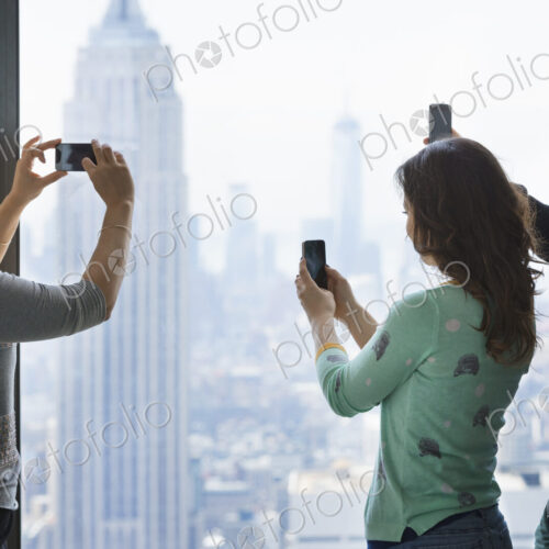 Urban lifestyle. Three people standing on an observation deck, using their phones to… Urban lifestyle. Three people standing on an observation deck, using their phones to…