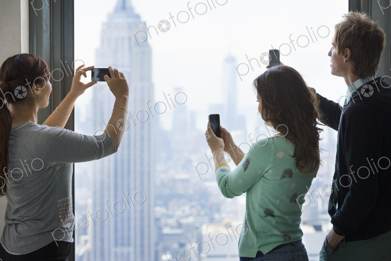 Urban lifestyle. Three people standing on an observation deck, using their phones to…