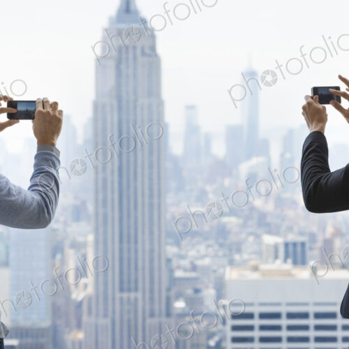 Urban lifestyle. Two young men using their phones to take images of the city from an… Urban lifestyle. Two young men using their phones to take images of the city from an…