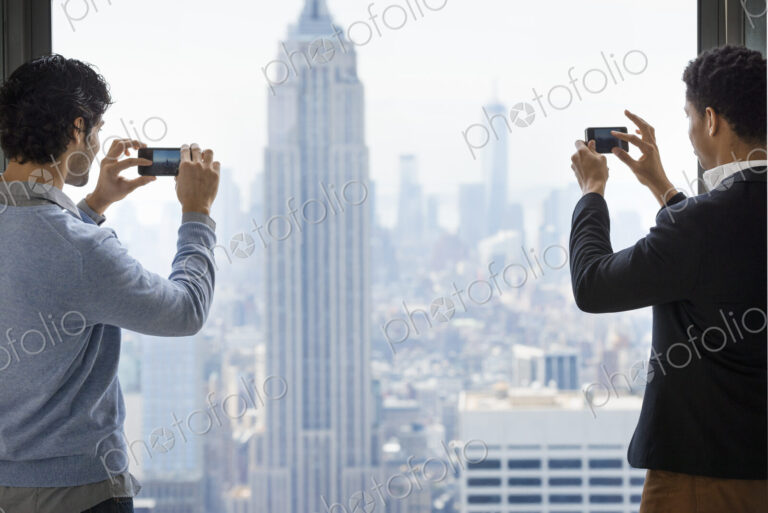 Urban lifestyle. Two young men using their phones to take images of the city from an…