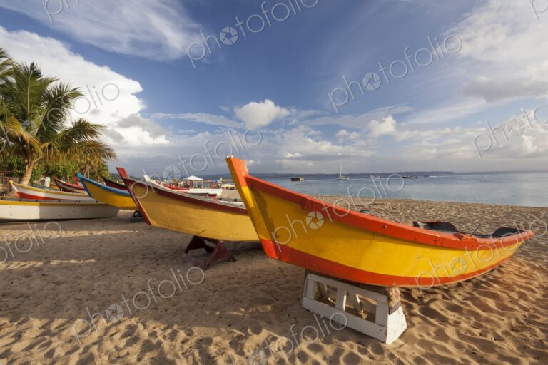 Vibrantly painted wooden fishing boats rest on the golden sand of Crash Boat Beach in…
