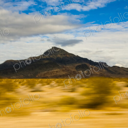 View across a desert landscape to a sharp peak, seen from a moving vehicle. View across a desert landscape to a sharp peak, seen from a moving vehicle.