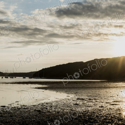 View across a sandy beach towards sailboats and distant cliffs at sunset. View across a sandy beach towards sailboats and distant cliffs at sunset.