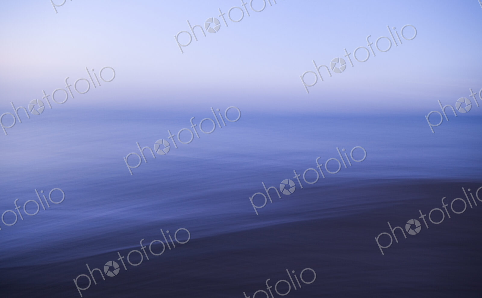 View across a seascape to the horizon, flat calm water surface and blurred motion.