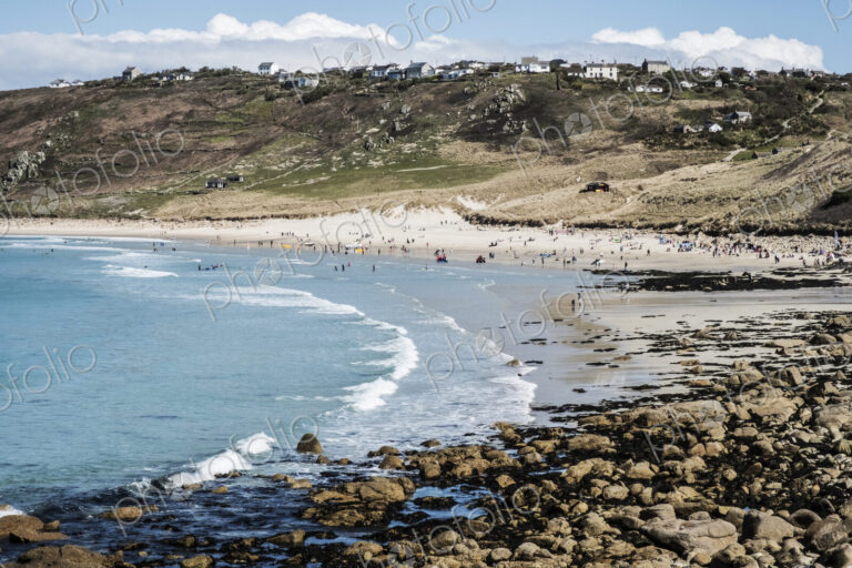 View along a coastline and sandy beach, waves breaking and people on the shore, with…