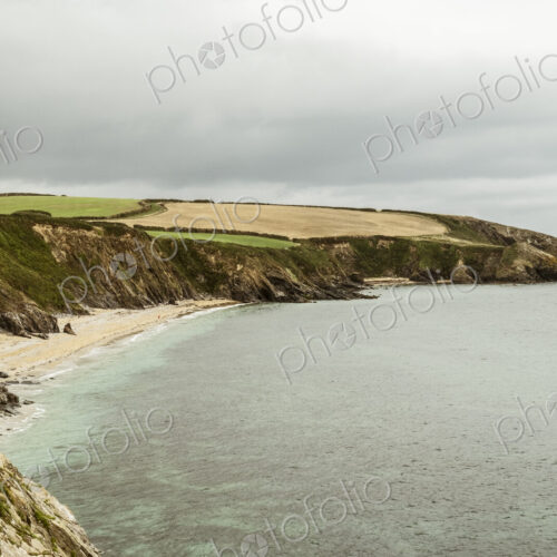 View along a coastline with cliffs and sandy beach and a headland, overcast grey skies.