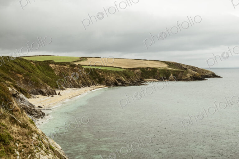 View along a coastline with cliffs and sandy beach and a headland, overcast grey skies.