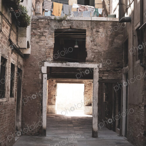 View along a narrow alley with residential buildings and gateway in Venice, Veneto, Italy.