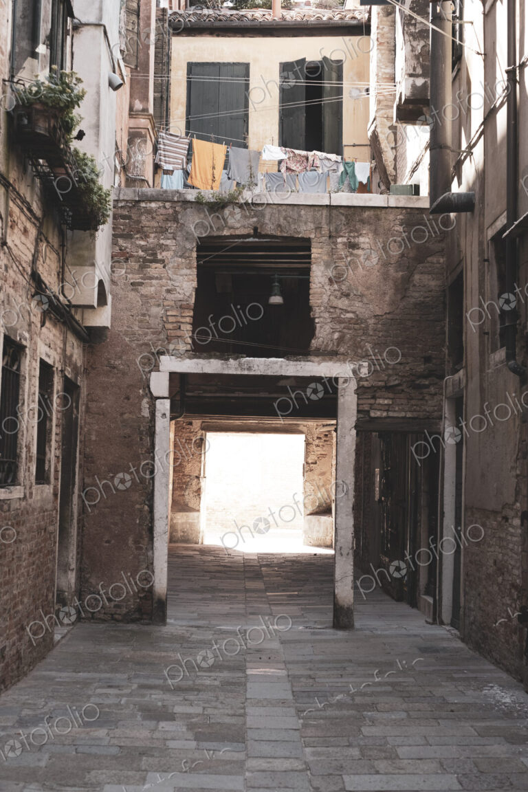 View along a narrow alley with residential buildings and gateway in Venice, Veneto, Italy.