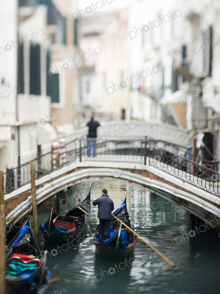 View along a narrow canal, with a person standing on a bridge. A gondola floating below.