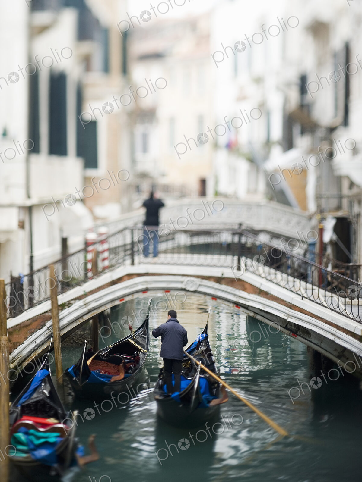 View along a narrow canal, with a person standing on a bridge. A gondola floating below.