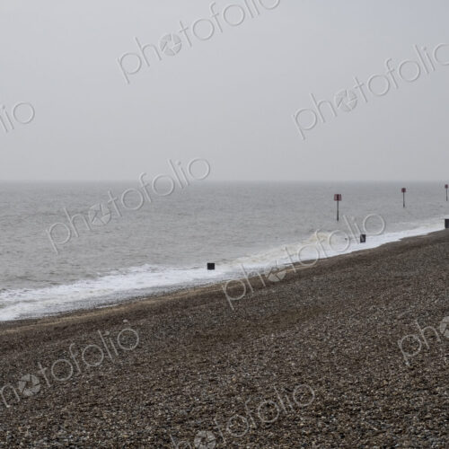 View along shingle beach with a row of partially submerged metal marker poles in the… View along shingle beach with a row of partially submerged metal marker poles in the…
