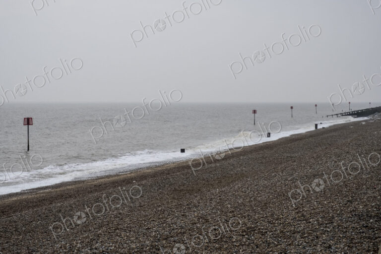 View along shingle beach with a row of partially submerged metal marker poles in the…