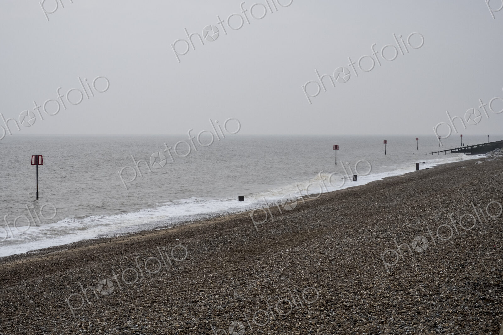 View along shingle beach with a row of partially submerged metal marker poles in the…