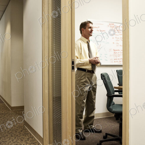 View down a hallway with a caucasian man in a meeting in an office.