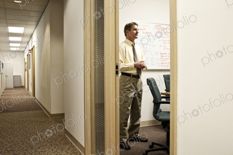 View down a hallway with a caucasian man in a meeting in an office.