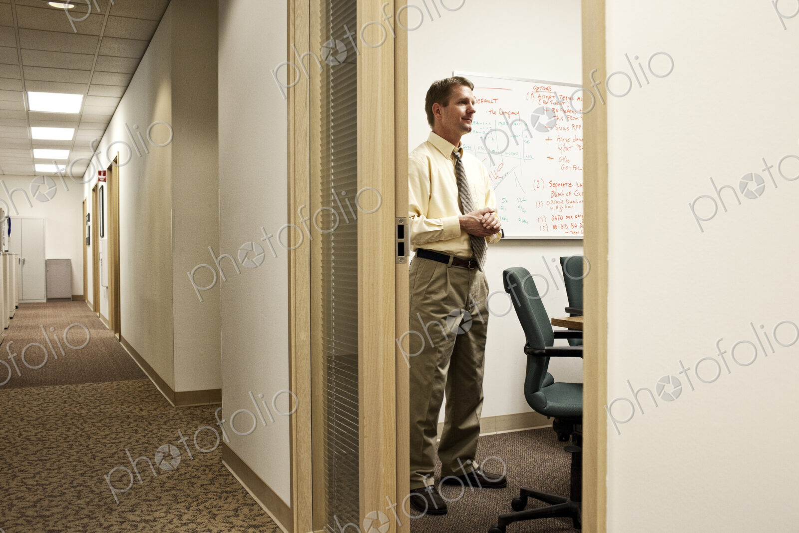 View down a hallway with a caucasian man in a meeting in an office.