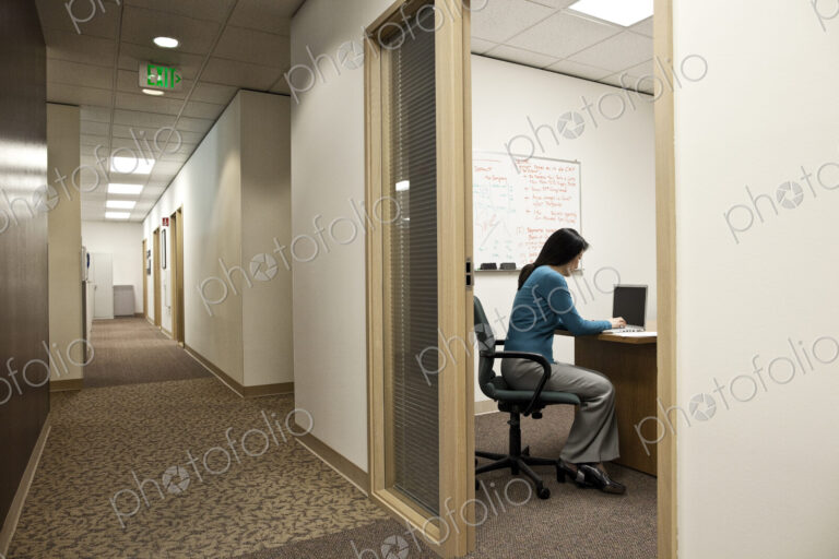 View down a hallway with an asian woman in a meeting in an office.