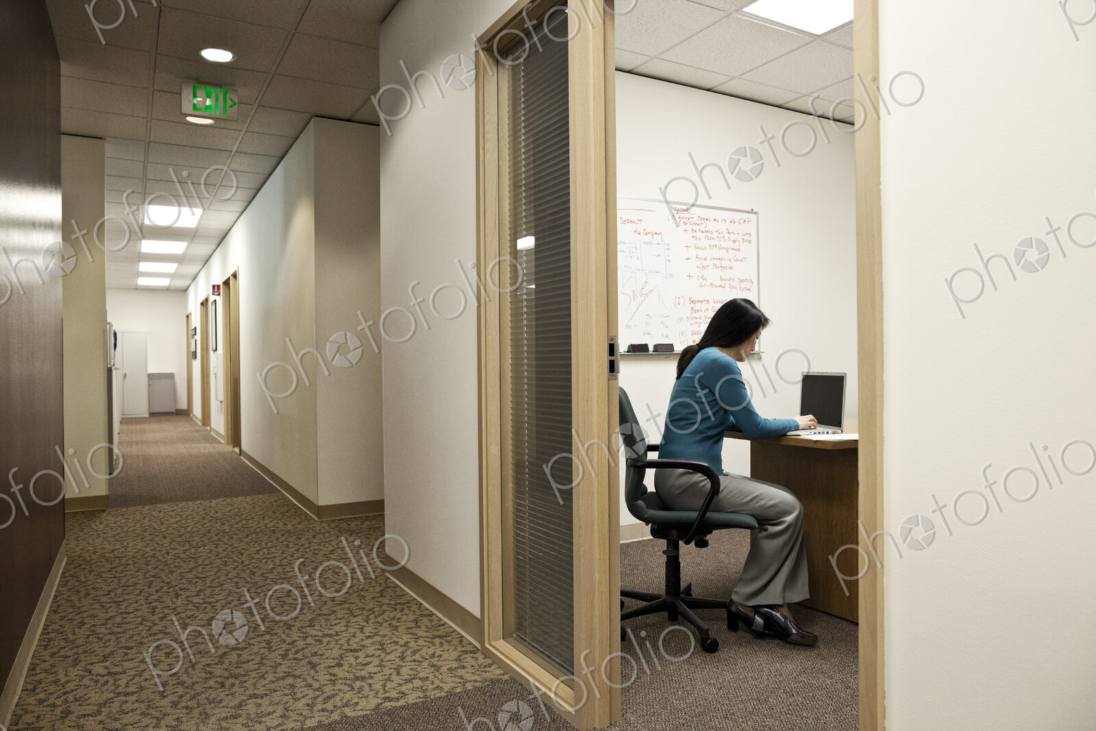 View down a hallway with an asian woman in a meeting in an office.