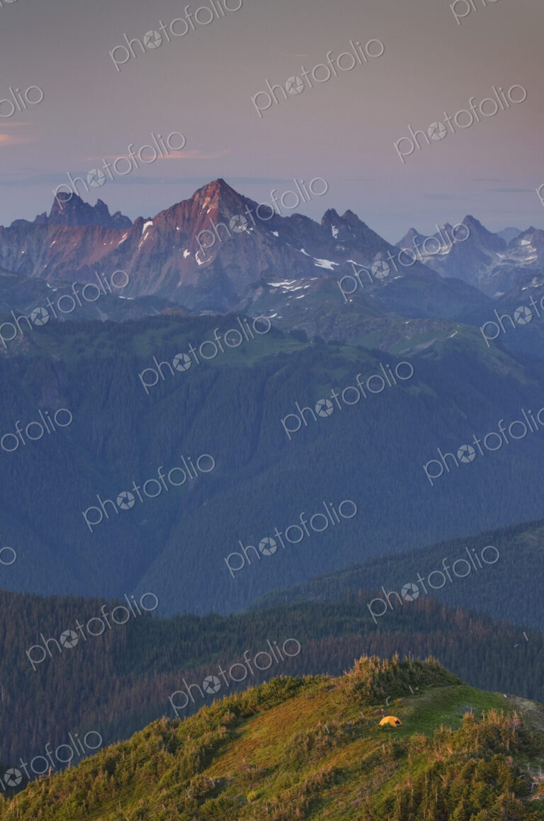 View from above, a small orange tent pitched on a ridge, with views into the valley…