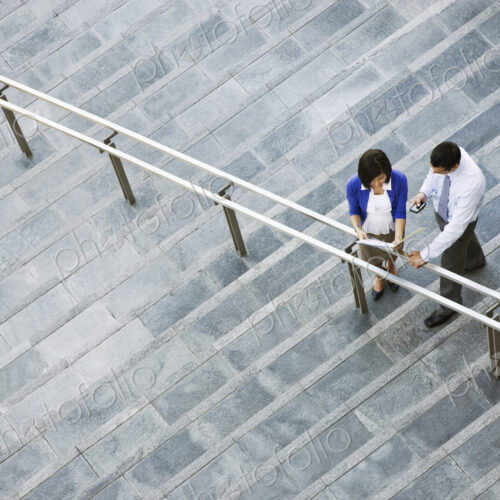 View from above looking down on a businesswoman and businessman standing on steps up…