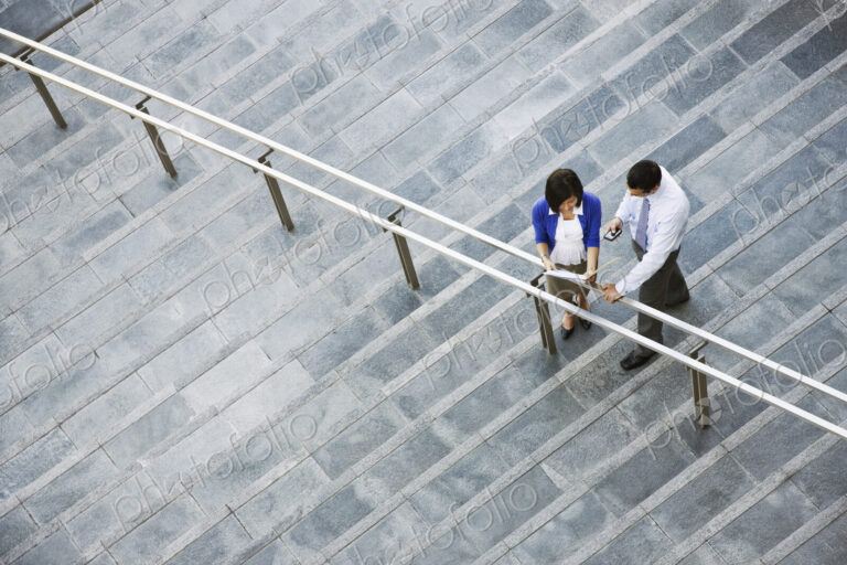 View from above looking down on a businesswoman and businessman standing on steps up…