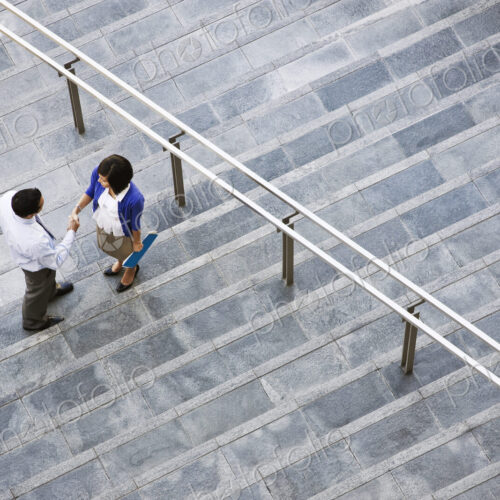 View from above looking down on a businesswoman and businessman standing on steps up…