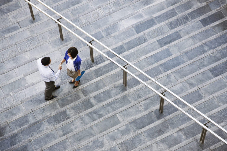 View from above looking down on a businesswoman and businessman standing on steps up…