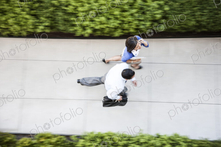 View from above of a businessman and woman walking on a sidewalk.
