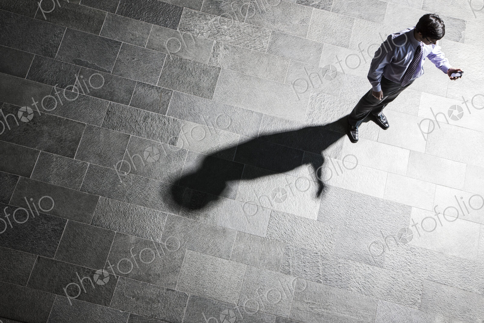 View from above of a businessman checking his phone and his shadow on the lobby floor.