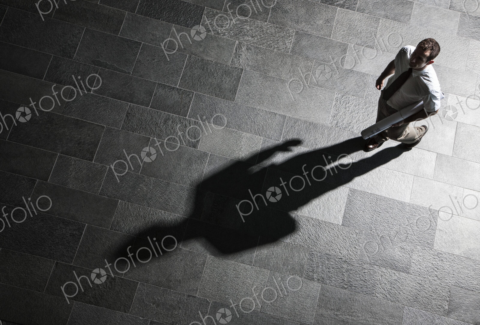 View from above of a businessman walking across a lobby floor and a shadow on the floor.