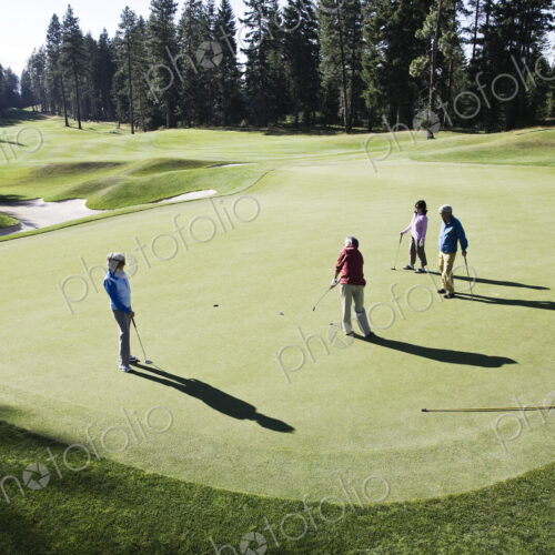 View from above of four golfers playing golf on a green in the distance. View from above of four golfers playing golf on a green in the distance.