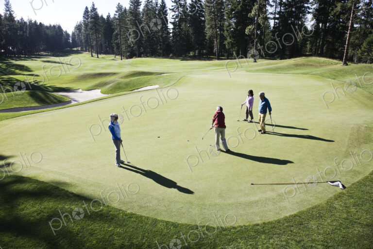 View from above of four golfers playing golf on a green in the distance.
