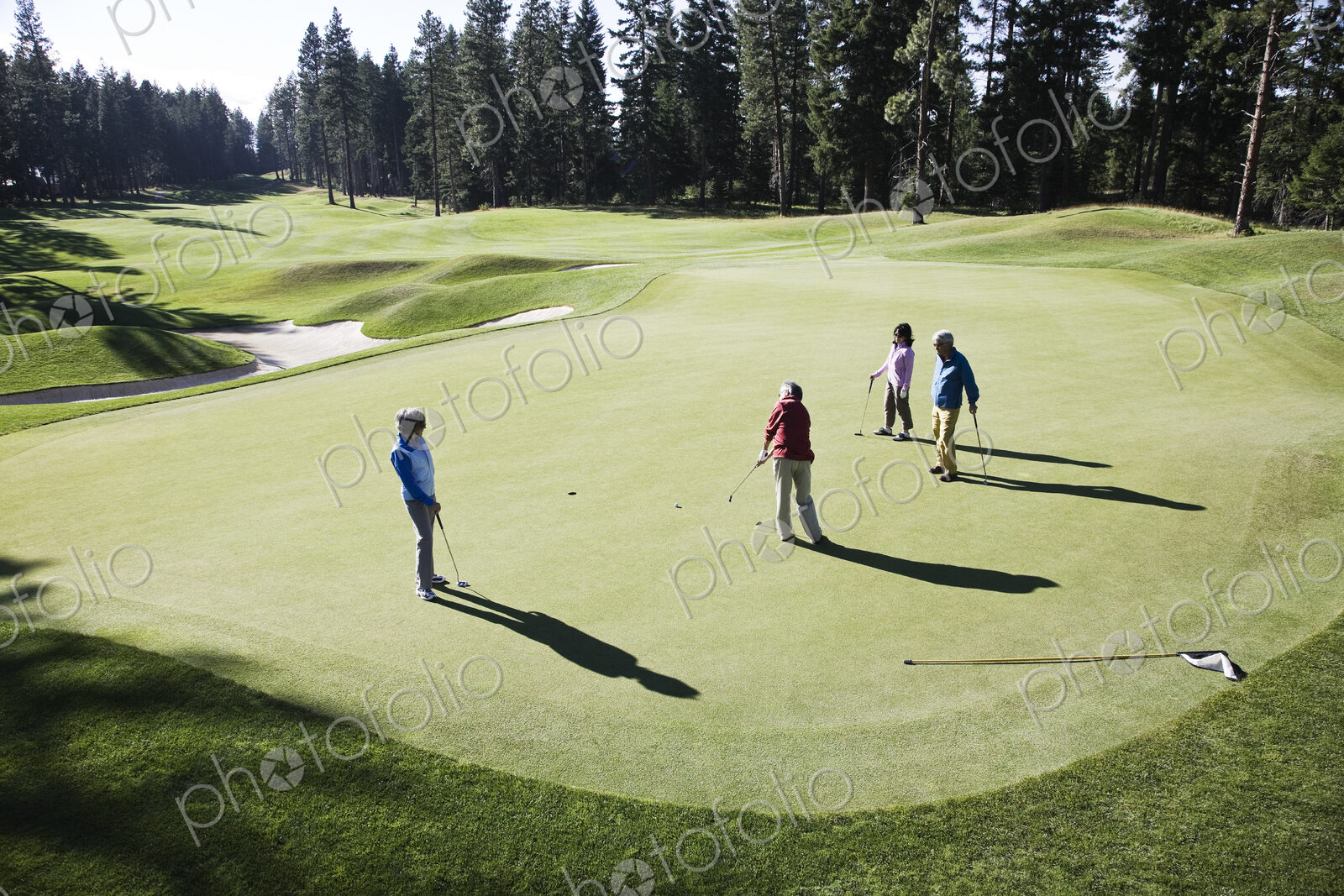 View from above of four golfers playing golf on a green in the distance.