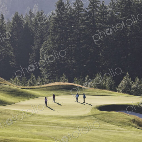 View from above of four golfers playing golf on a green in the distance. View from above of four golfers playing golf on a green in the distance.
