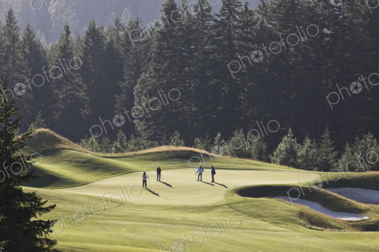 View from above of four golfers playing golf on a green in the distance.