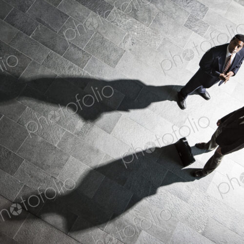 View from above of two businessmen and shadows on the floor of a business lobby. View from above of two businessmen and shadows on the floor of a business lobby.