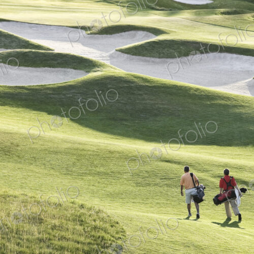View from above of two golfers walking on a fairway toward the greeen of a golf course. View from above of two golfers walking on a fairway toward the greeen of a golf course.