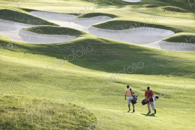View from above of two golfers walking on a fairway toward the greeen of a golf course.