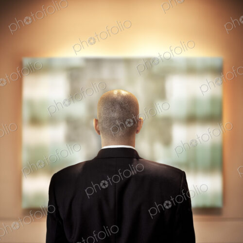 View from behid of a businessman looking at a piece of art in a gallery. View from behid of a businessman looking at a piece of art in a gallery.