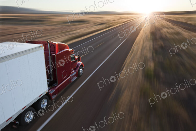 View from behind and above a commercial truck on the road at sunset on a highway in…