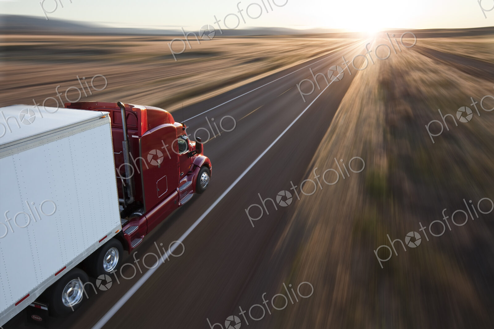 View from behind and above a commercial truck on the road at sunset on a highway in…
