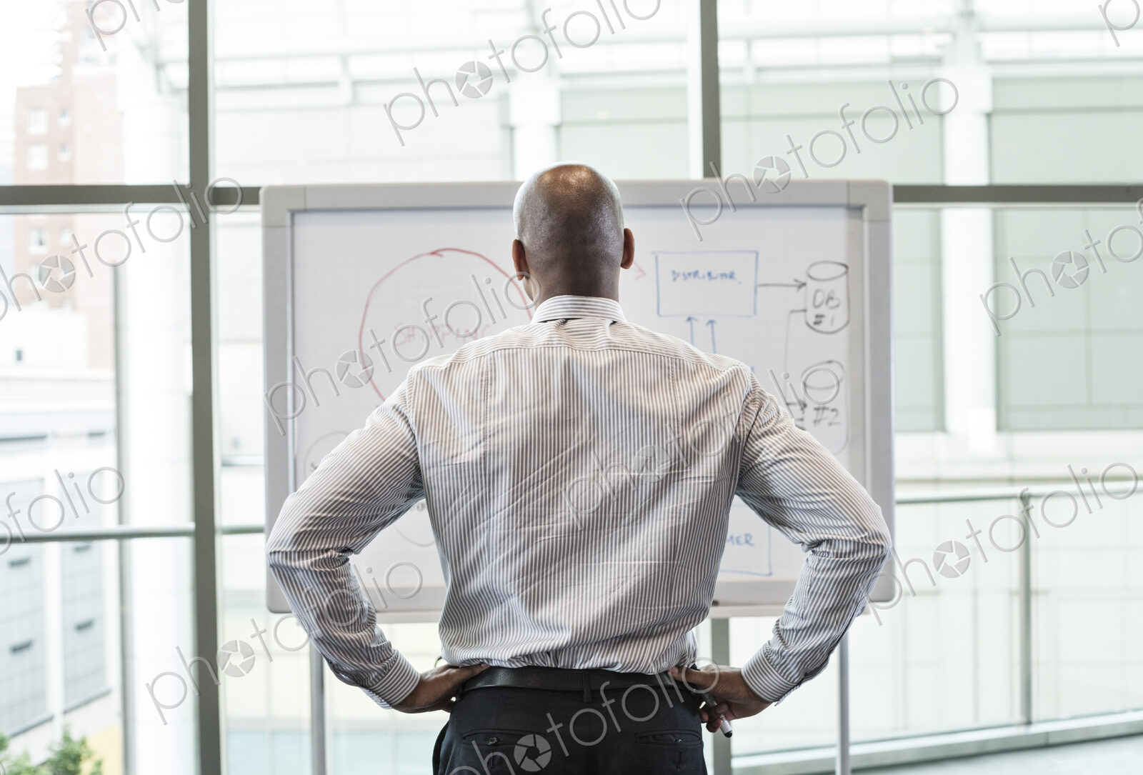 View from behind of a businessman standing at a white board in front of a large window.