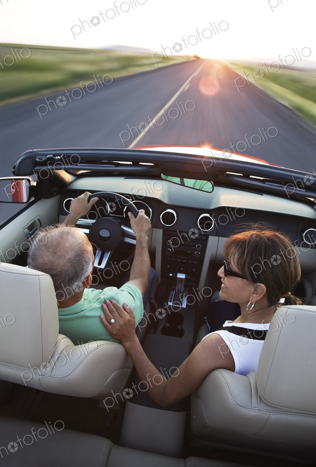 View from behind of a senior couple in a convertible sports car driving on a highway…