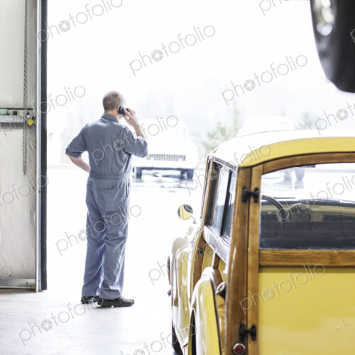 View from behind of an owner of a car repair shop on his cell phone.