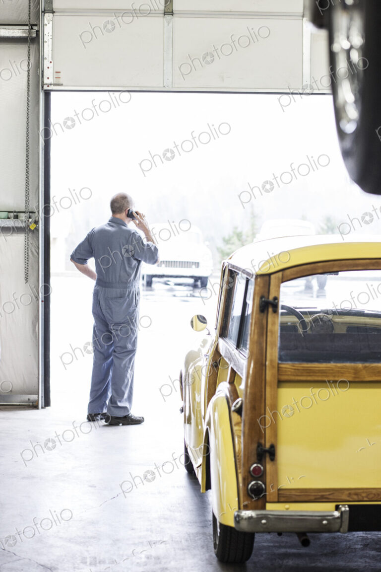 View from behind of an owner of a car repair shop on his cell phone.