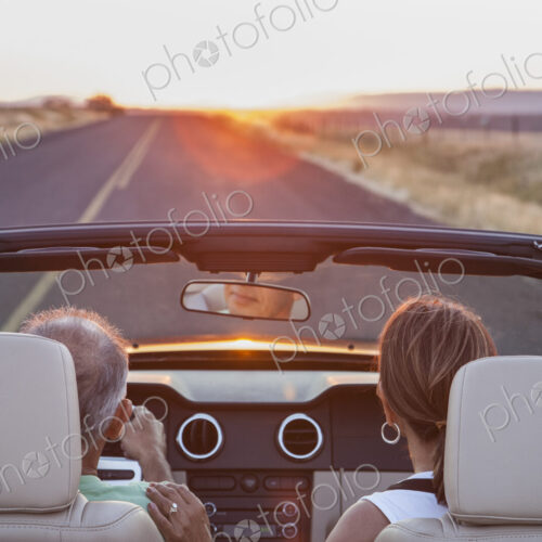 View from behind of senior couple in a convertible sports car driving on a highway at…