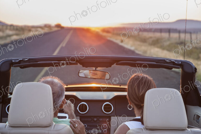 View from behind of senior couple in a convertible sports car driving on a highway at…