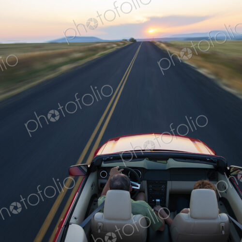 View from behind of senior couple in a convertible sports car driving on a highway at…